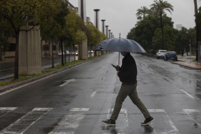 Archivo - Un hombre camina protegido de la lluvia con un paraguas
