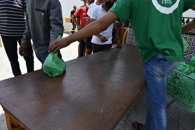 Un miembro de la asociación islámica 'Luna Blanca' reparte una bolsa de comida a varios migrantes en Ceuta (España), en una imagen de la pasada semana