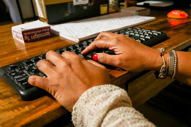 Archivo - Unas manos de mujer escriben en el teclado de un ordenador, sobre una mesa de madera.