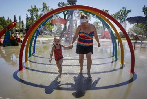 Una madre y su hija corren entre aspersores para tratar de vencer el calor en un parque. - Jeff Mcintosh/The Canadian Press / DPA