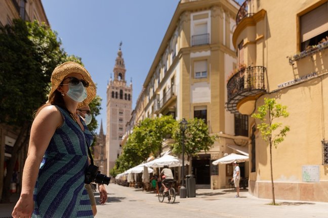 Turistas pasean por el centro de Sevilla provistos de gorras, abanicos y botellas de agua 