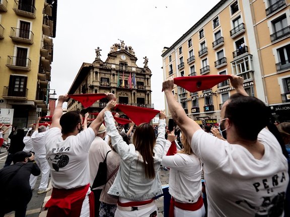 Varias personas levantan los pañuelos rojos a las 12 del mediodía en la plaza del Ayuntamiento de Pamplona, momento en que habría tenido lugar el tradicional chupinazo de San Fermín, suspendidos por segundo año por la pandemia