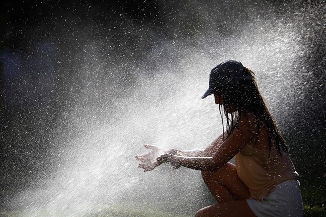 Una joven trata de mitigar los altas temperaturas que se alcanzarán este domingo en Córdoba, superiores a 40 grados, refrescándose con los aspersores de riego de un parque. EFE/Salas