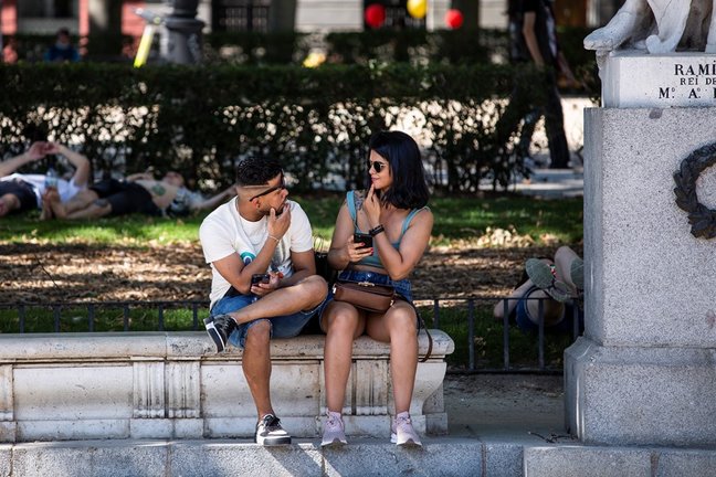 Dos personas sin mascarilla, sentadas en un banco de la Plaza de Oriente