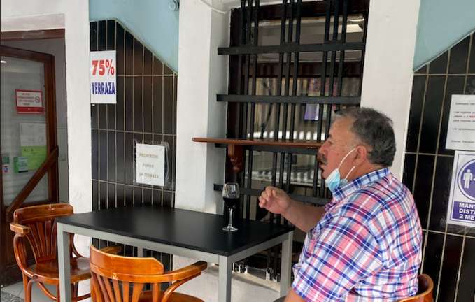 Un hombre toma un vino en una terraza en Santander bajo el cartel de 75% de aforno.  / ALERTA