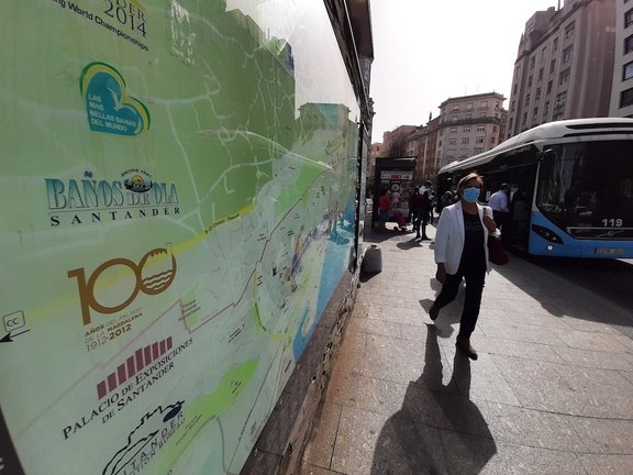 Una persona con mascarilla sale de un autobús en la parada del Ayuntamiento frente a un cartel de turismo de la ciudad. / S. Díaz