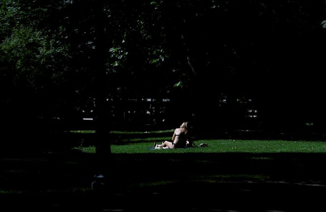 Archivo - Una joven toma el sol en el césped en el Parque del Retiro en Madrid.