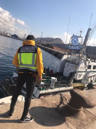 Un agente observa un barco en el que se encuentran varias personas inmigrantes