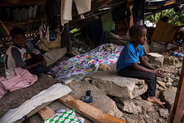 Niños permanecen protegidos en los restos de su hogar cuando se registran lluvias que deja el paso de la tormenta Grace, este martes en Camp Perrin (Haití). Fuertes lluvias cayeron en las últimas horas en el suroeste de Haití, la zona más afectada por el terremoto de magnitud 7,2 en la escala Richter que el sábado pasado causó más de 1.400 muertos y 6.900 heridos. EFE/ Orlando Barría