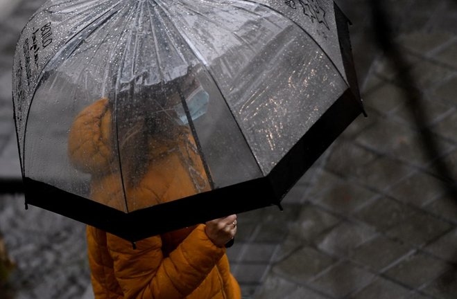 Archivo - Una persona caminando bajo un paraguas para protegerse de la lluvia en Madrid