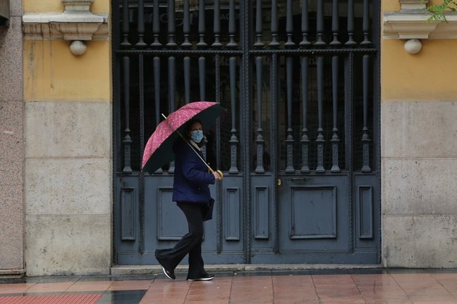 Archivo - Una mujer pasa frente a una puerta en la capital en un día de lluvia  