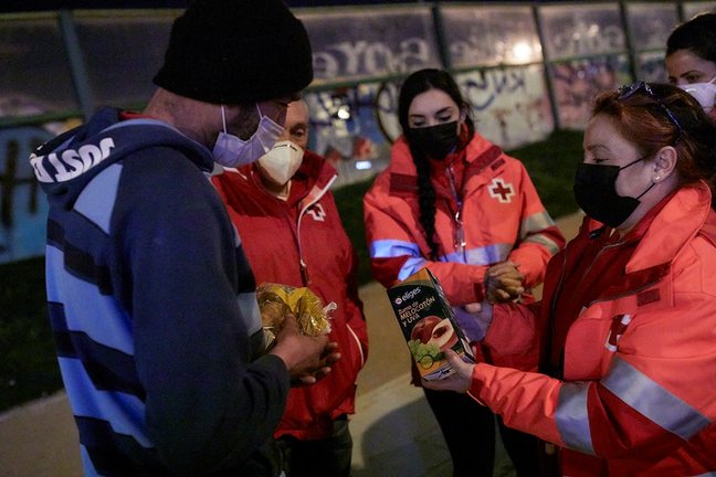Archivo - Varios trabajadores de Cruz Roja ofrecen comida a un hombre sin hogar