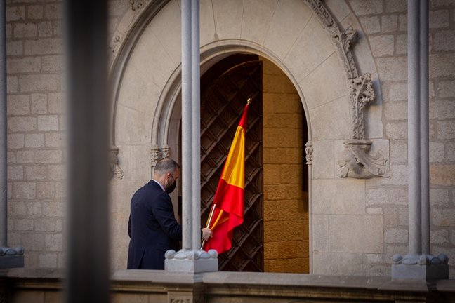 Un hombre retira la bandera de España antes de que el president de la Generalitat comparezca en rueda de prensa en el Palau de la Generalitat
