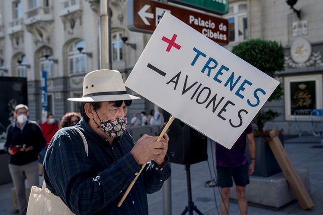Una mujer sostiene una pancarta donde se lee "Más trenes, menos aviones", en una concentración contra la ampliación del aeropuerto Adolfo Suárez Madrid-Barajas.