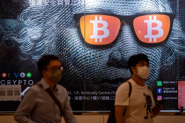 Dos hombres pasan junto a un cartel publicitario de Bitcoins y criptomonedas en Hong Kong, China, el 25 de septiembre de 2021. El 24 de septiembre, China intensificó la represión de las criptomonedas con una prohibición general de todas las transacciones de criptomonedas, afectando a bitcoin y otras monedas importantes. EFE/EPA/JEROME FAVRE