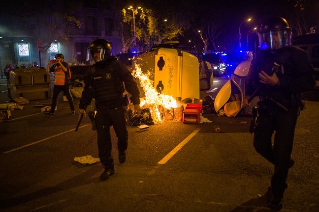 Varios mossos antidisturbios pasan delante de un contenedor quemado en la plaza Urquinaona durante una manifestación por el referéndum del 1-O en Catalunya, a 1 de octubre de 2021, en Barcelona
