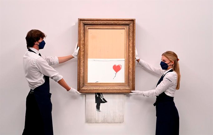 Empleados de la galería posan para los fotógrafos junto a un cuadro titulado "El amor está en la papelera" del artista callejero británico anónimo Banksy en la casa de subastas Sotheby's en Londres, Gran Bretaña 03 de septiembre de 2021