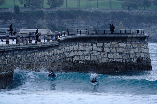 Varios surfistas cabalgan una ola en la playa del Sardinero de Santander. / Hardy