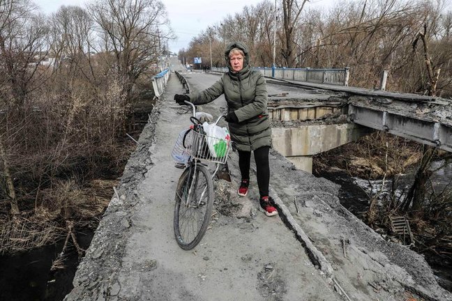 Una mujer pasa con su bicicleta por los restos del puente principal de la ciudad de Malyn, destruido tras el bombardeo de la aviación rusa, en Malyn, Ucrania, el 12 de marzo de 2022. EFE/EPA/MIGUEL A. LOPES