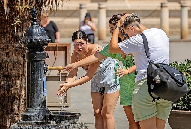 Unas turistas se refrescan en una fuente de agua junto a la Catedral de Sevilla ayer viernes a mediodía. / EFE/Julio Muñoz