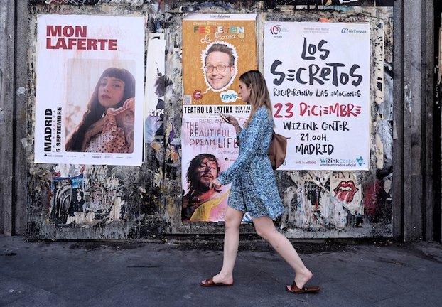 Una mujer pasa con su teléfono móvil por varios carteles de conciertos, a 26 de julio de 2022, en Madrid (España). / Eduardo Parra / E.P.
