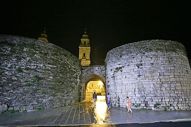 Varias personas caminan por la muralla romana de Lugo sin iluminación, tras las medidas de ahorro energético del Gobierno central. /Carlos Castro