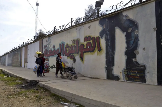 Tres niños caminan junto a un muro con eslóganes del grupo yihadista Estado Islámico (EI)