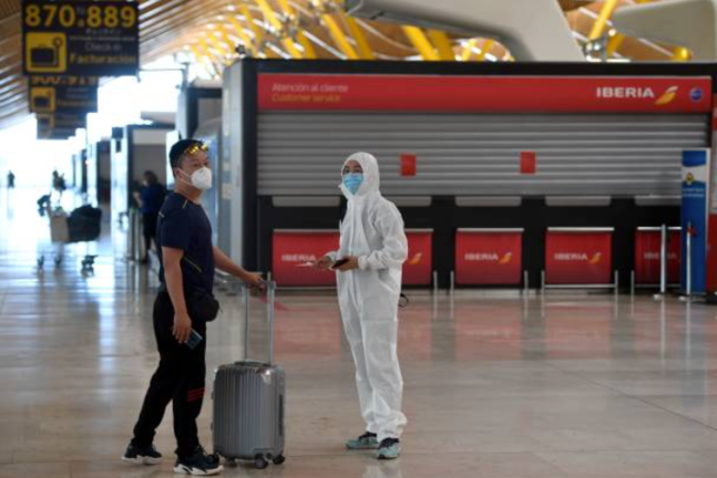Un pasajero ataviado con un traje de protección espera junto a un familiar tras facturar un vuelo con destino a Pekín en el aeropuerto de Barajas. / E.P.