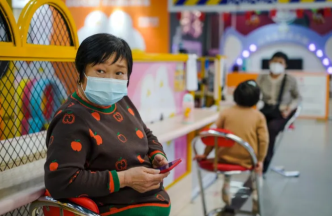 Una mujer protegida con una mascarilla utiliza su móvil en un centro comercial de Pekín el pasado 11 de enero. EFE / Wu Hao