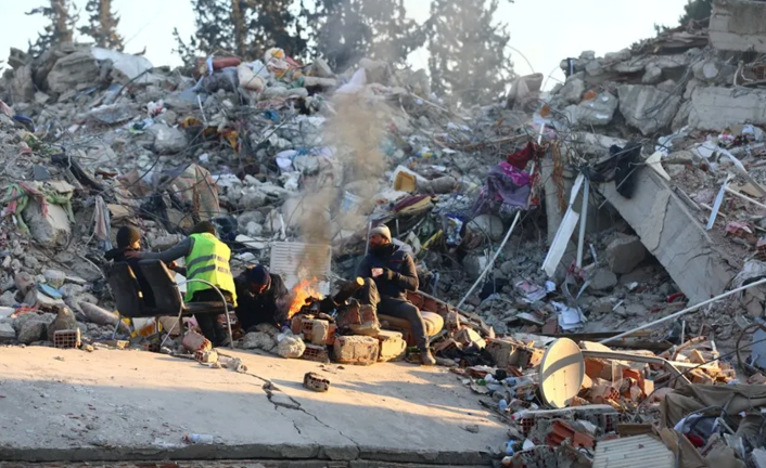 Familiares de personas desaparecidas se calientan alrededor de una hoguera encendida sobre los escombros de un edificio derrumbado por el terremoto. EFE / Tolga Bozoglu