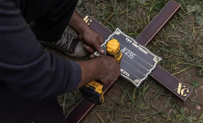Un trabajador coloca una placa con un número en una cruz durante el entierro masivo de personas no identificadas que fueron asesinadas en el distrito de Bucha al noroeste de Kiev, en agosto de 2022. EFE/EPA/Roman Pilipey