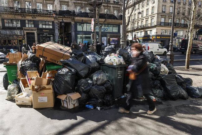 Una mujer camina frente a varias bolsas de basura en París. EFE / Mohammed Badra