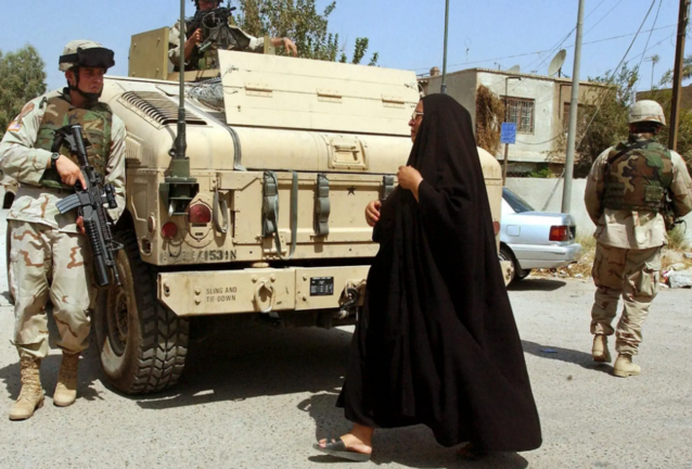 Fotografía fechada el 8 de septiembre de 2004 que muestra a una mujer iraquí que se cruza con soldados estadounidenses que patrullan las calles de Bagdad (Irak). EFE/Mohammed Messara