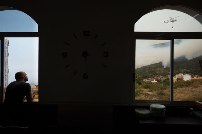 Un hombre observa desde una ventana de un restaurante de Aguamansa, en el municipio de La Orotava, los trabajos de los helicópteros que trabajan en la extinción del incendio forestal. EFE / Ramón de la Rocha