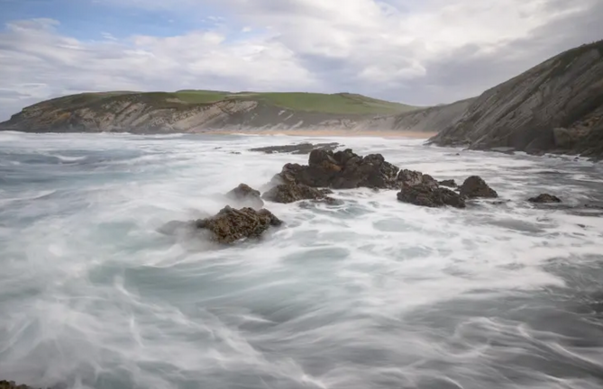 Una ola rompe sobre las rocas en la playa de Tagle
