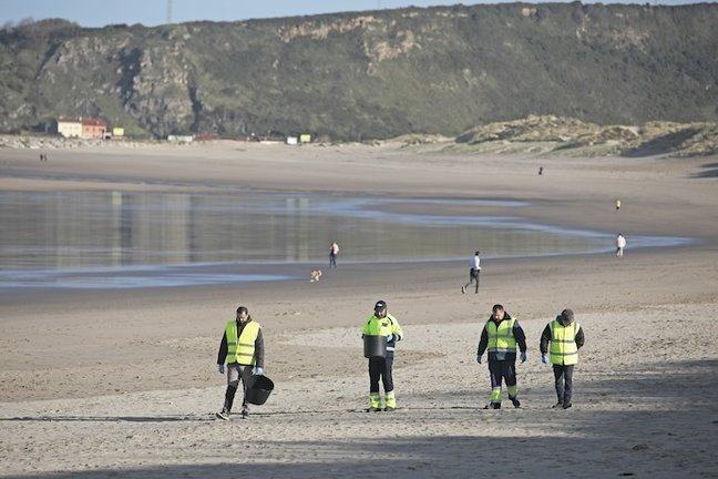 Operarios de la empresa TRAGSA realizan labores de recogida de "pellets" en la playa de Salinas. En Castrillón (Asturias), a 13/01/2023 (© Jorge Peteiro / Europa Press)
