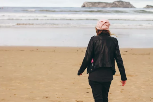 Una joven se envuelve en su abrigo mientras disfruta de un sereno paseo por una de las playas del Cantábrico, capturando un momento de paz y reflexión personal frente a la inmensidad del mar.