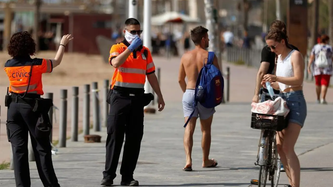 Agentes Civicos indican a una joven que se coloque la mascarilla protectora, este s&aacute;bado en el paseo mar&iacute;timo de la Barceloneta en Barcelona. EFE/Toni Albir