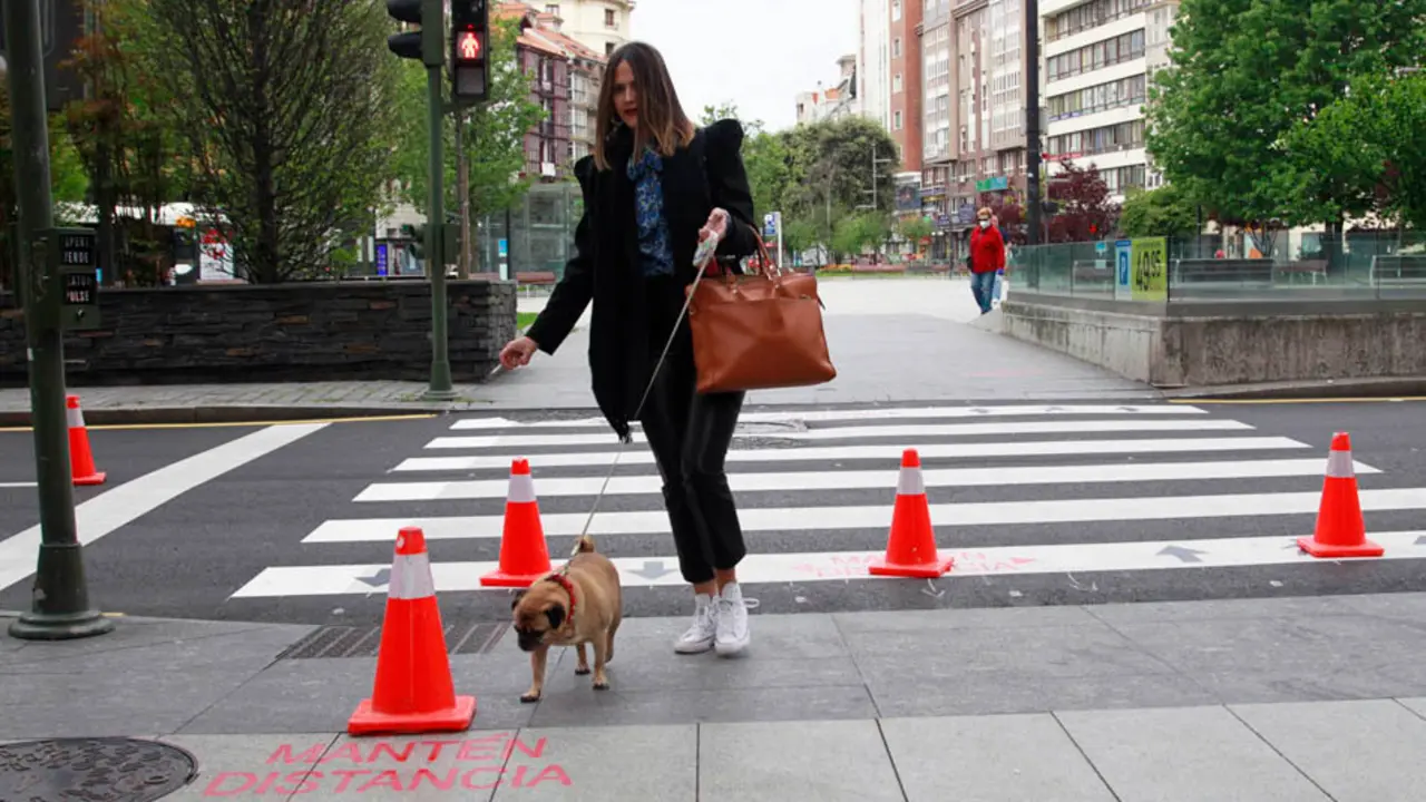 Una persona pasea por el paso de cebra junto a una pintada que se lee 'mantenga la distancia', en la calle Isabel II en Santander. / J. Ram&oacute;n