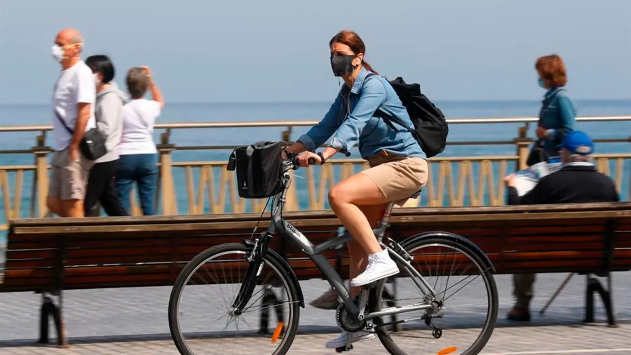 Una mujer pasea en bicicleta protegida con una mascarilla por el paseo de la Zurriola de San Sebasti&aacute;n. EFE/Juan Herrero/Archivo
