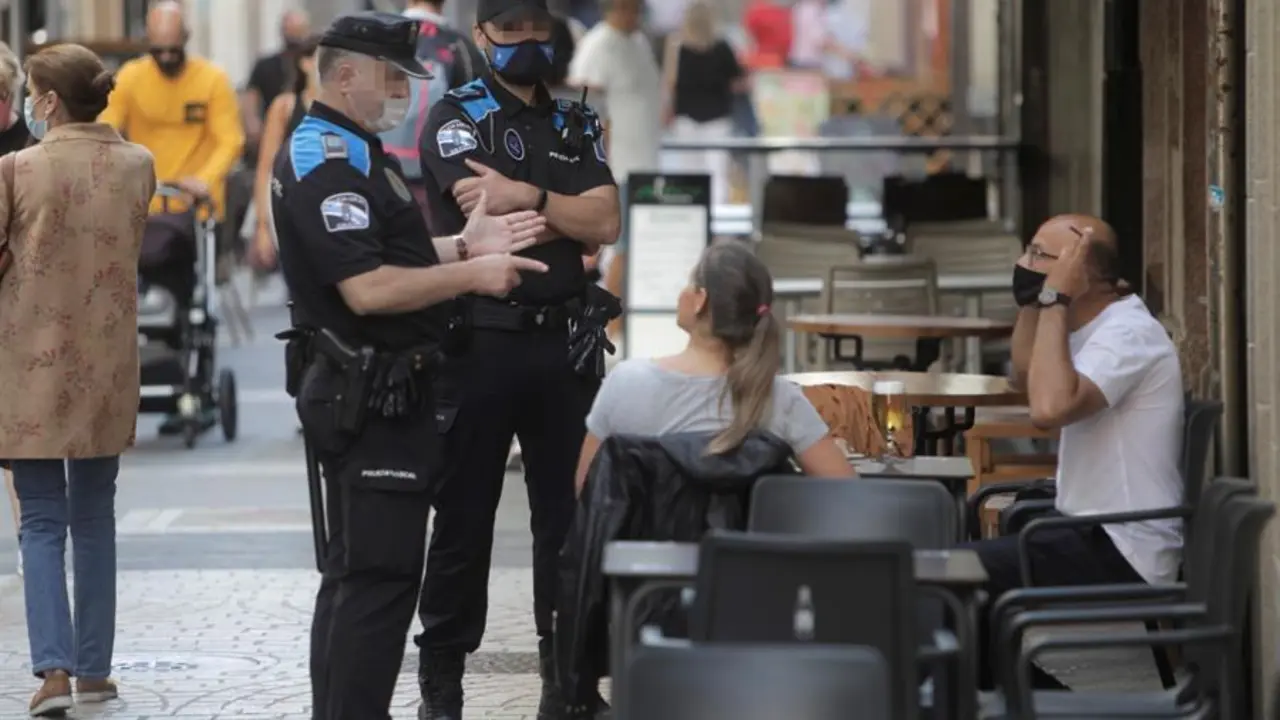 Dos agentes de la polic&iacute;a se dirigen a un hombre que se encontraba fumando en una terraza de un bar de la ciudad. EFE/ CABALAR