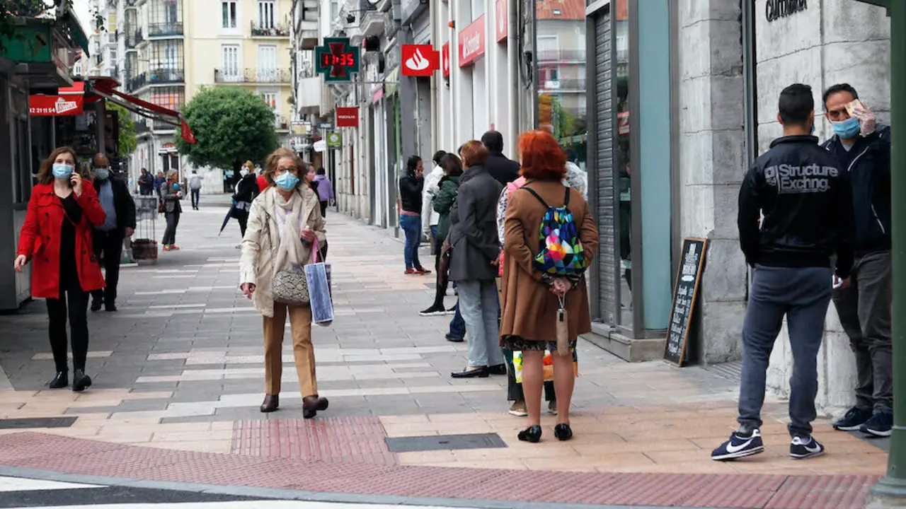 Varias personas con mascarilla hacen cola para entrar al banco. / J. R.