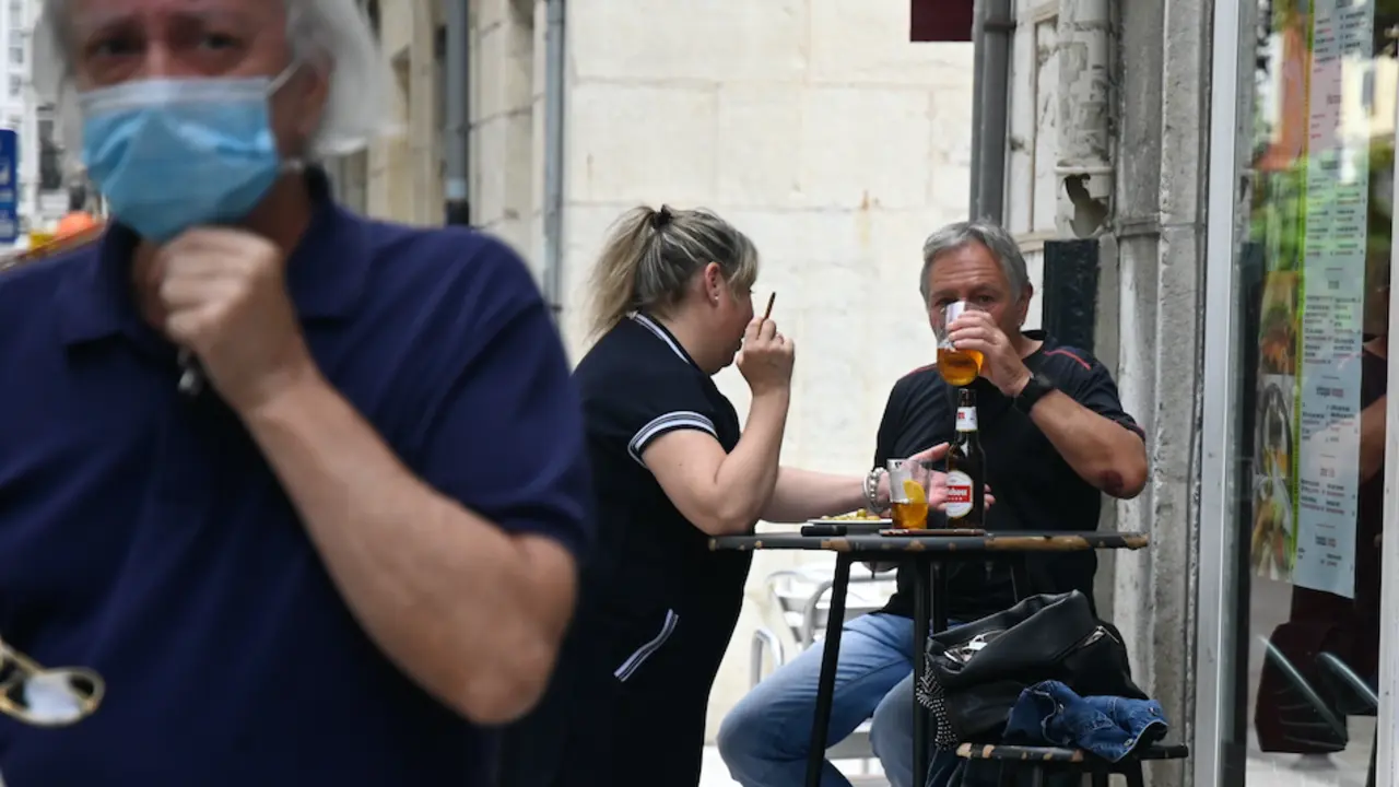 Una persona con mascarilla y al fondo una pareja tomando un refrigerio en una cafeter&iacute;a de Santander. / HARDY