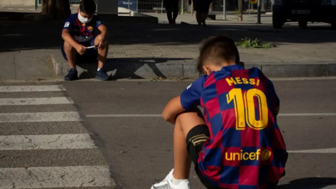Dos chicos esperan a la entrada de la ciudad deportiva Joan Gamper en Barcelona la llegada de los jugadores. Foto: EFE | Enric Fontcuberta