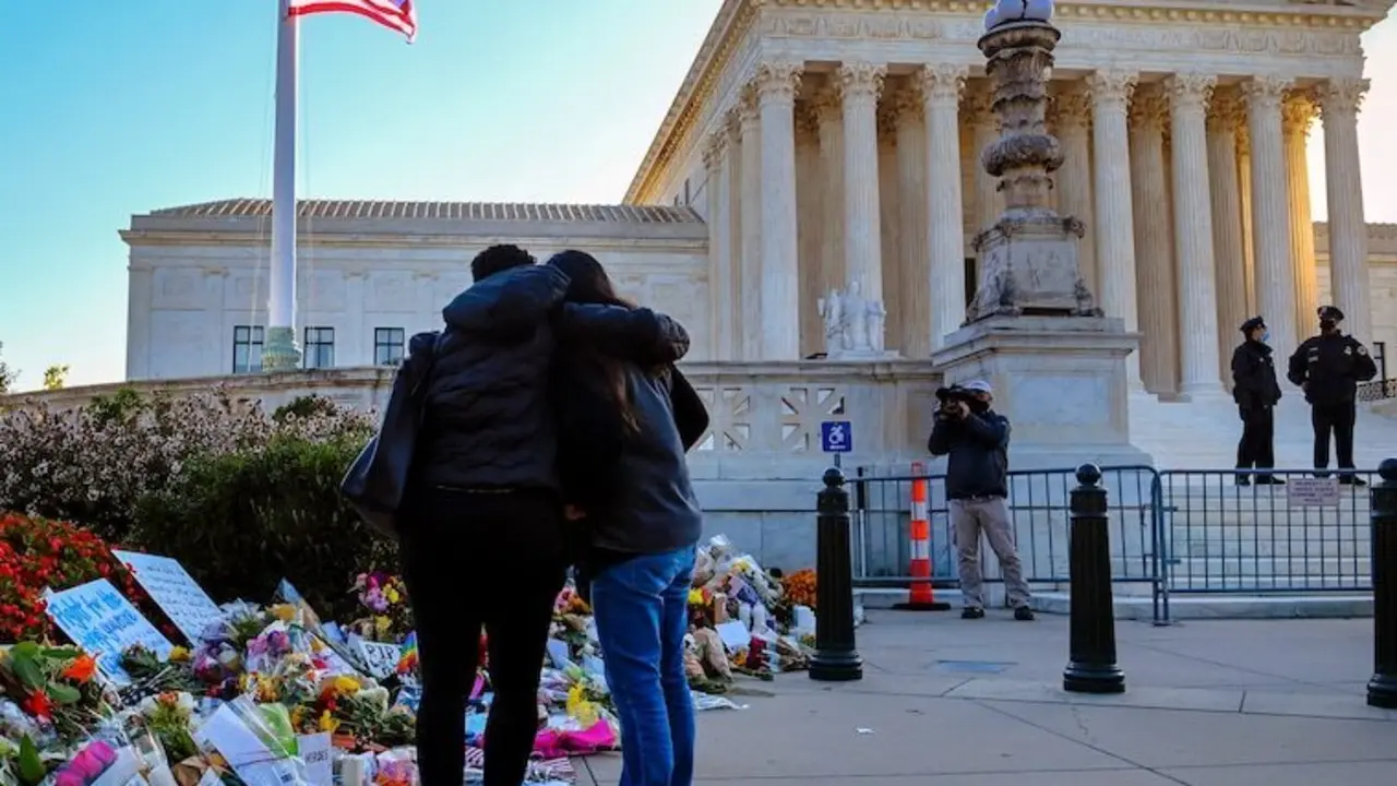 La bandera ondea a media asta y los visitantes examinan los recuerdos que se dejaron frente a la Corte Suprema la ma&ntilde;ana siguiente al anuncio de la muerte de la jueza Ruth Bader Ginsburg.