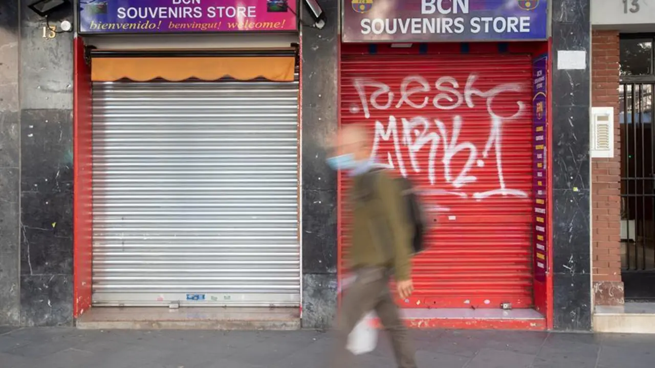 Un vecino pasa ante una tienda de recuerdos con la persiana bajada en un comercio cercano al Camp Nou. EFE/ Marta P&eacute;rez/Archivo