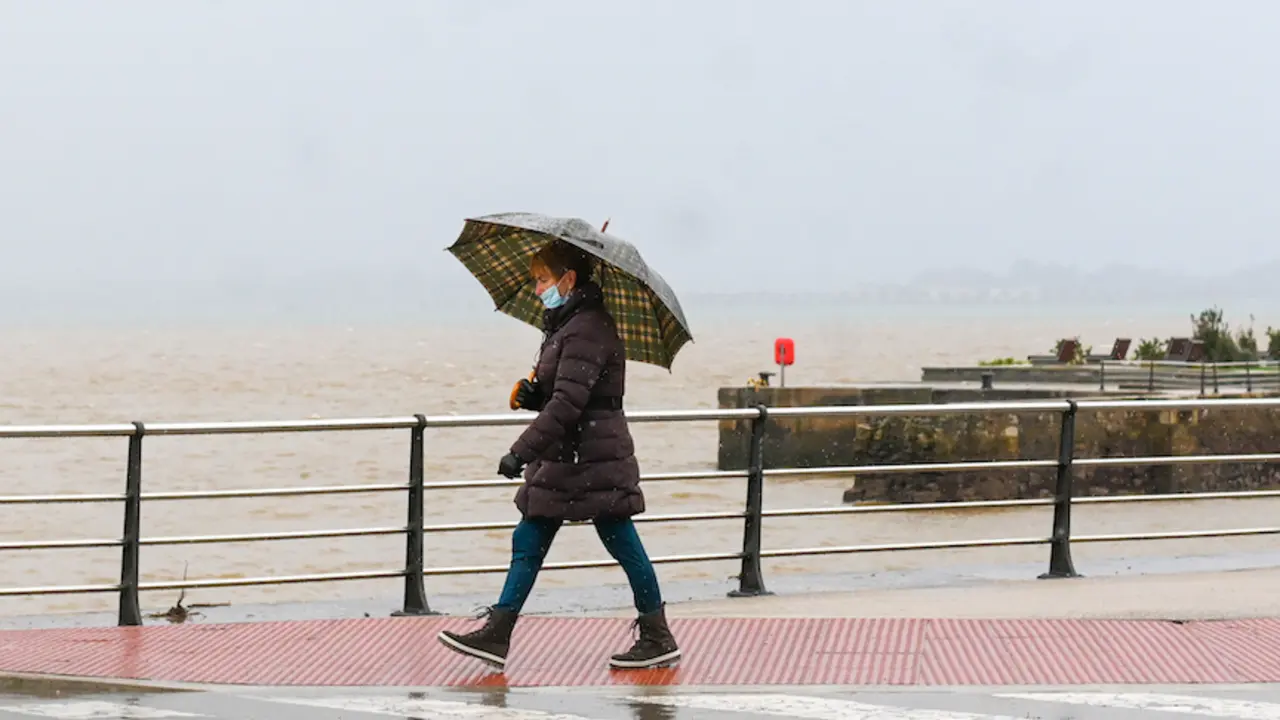 Una persona con su parag&uuml;as y mascarilla bajo la lluvia en Santander. / HARDY