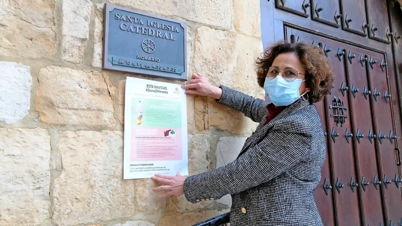 La directora de C&aacute;ritas, Sonsoles L&oacute;pez, colocando un cartel en la entrada de la Catedral de Santander. / ALERTA