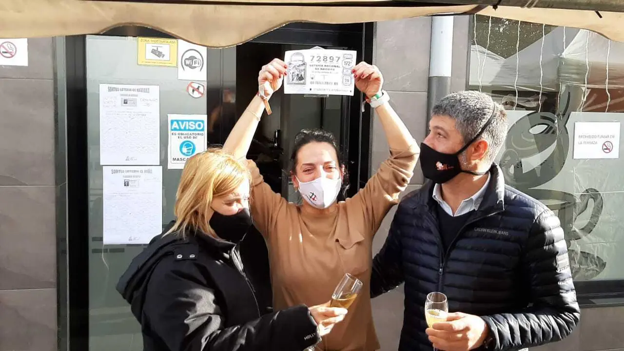 Luisa Ib&aacute;&ntilde;ez levanta el n&uacute;mero ganador del primer premio de la Loter&iacute;a mientras lo celebra con amigos y familiares. / ALERTA