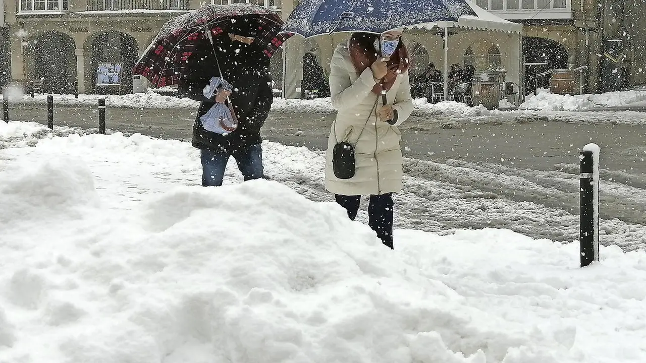 Dos personas caminan con su paraguas bajo la nieve en la localidad de Reinosa. / QUEIMADELOS